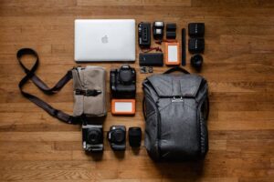 Cameras, laptop, bag, and backpack on a wooden surface.