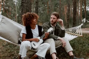 Two people relaxing in a hammock in the woods, with one playing a ukulele.