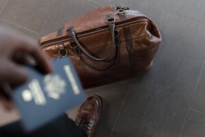 A travel bag on the floor with a person standing next to it holding a passport in their hand